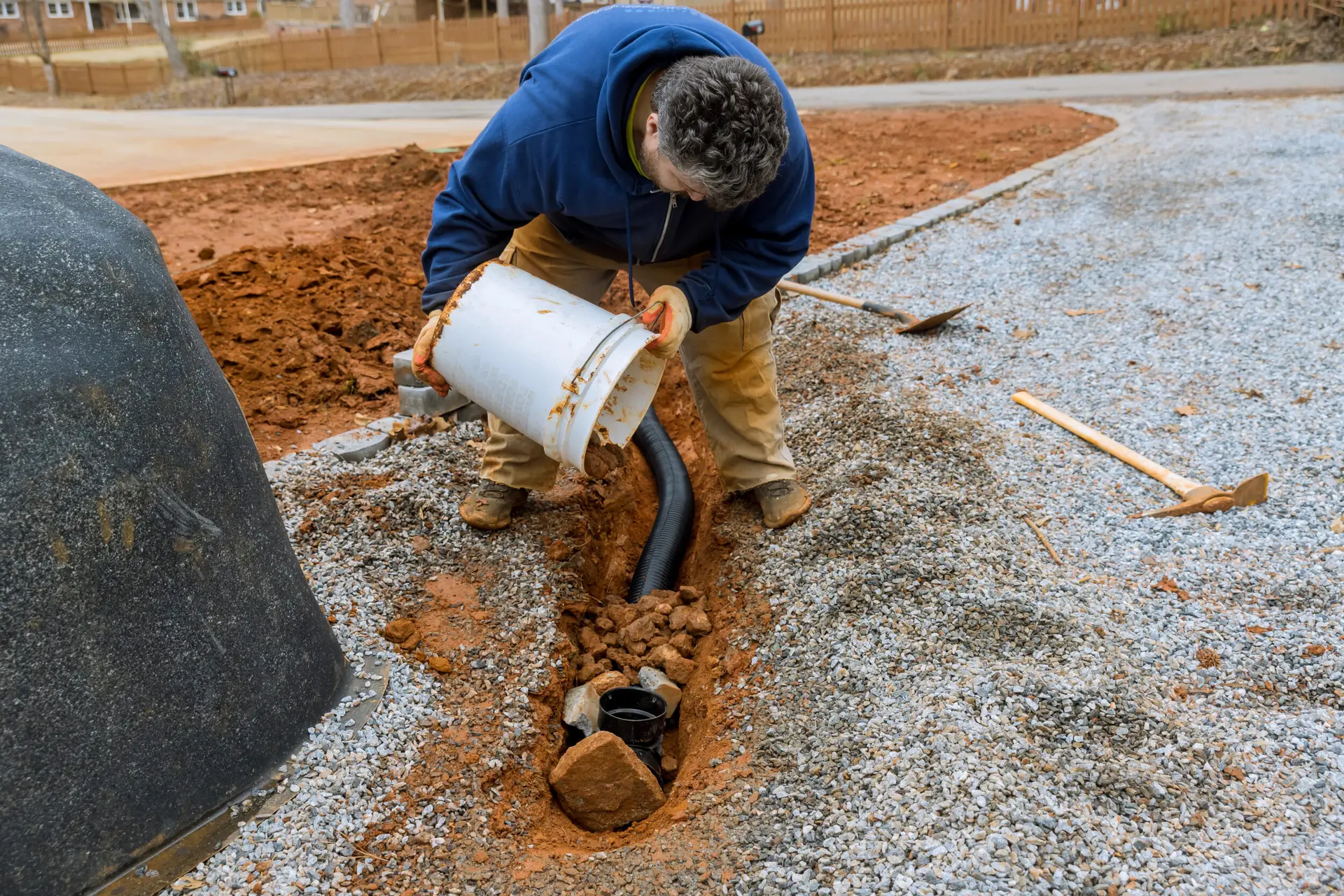 A Rhino Rooter worker gets a home ready for sewer repair by adding gravel around a new drainage pipe.