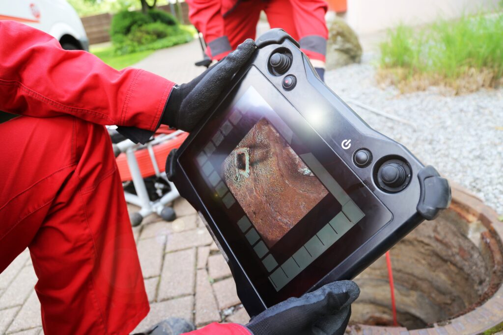 A Rhino Rooter technician in West Haven, Utah uses a tablet to check sewer and drain repairs during an outdoor inspection.