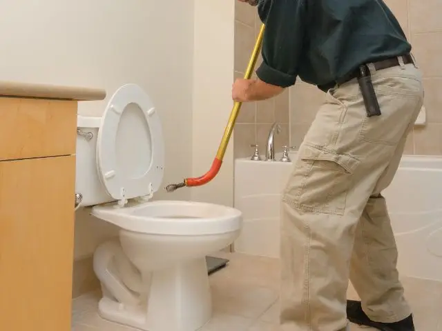 A Rhino Rooter worker unclogs a toilet, showing the service fixing bathroom plumbing problems for customers.