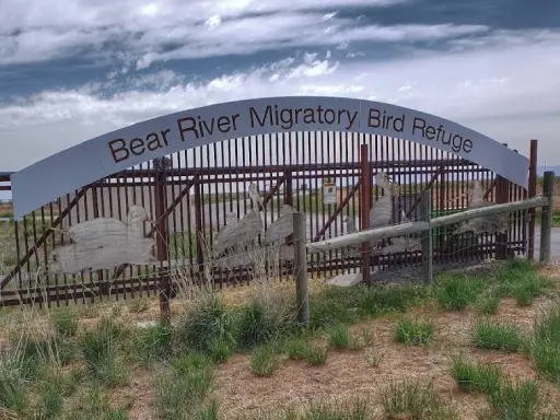 A metal sign welcomes visitors to Bear River Migratory Bird Refuge. The entrance looks inviting and highlights the area’s focus on nature.