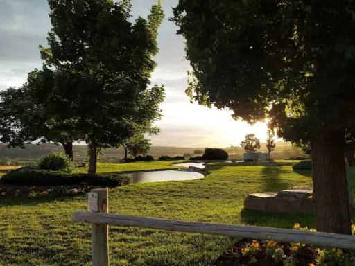 A peaceful park at sunset with a pond, green grass, and a fence like those Rhino Rooter helps keep clean.