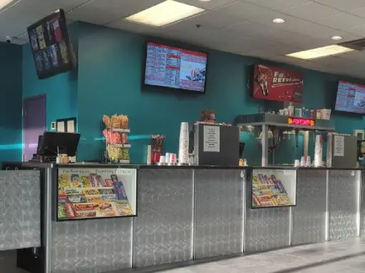 A busy theater snack counter with a friendly Rhino Rooter team member serving customers and bright menu signs showing available treats.