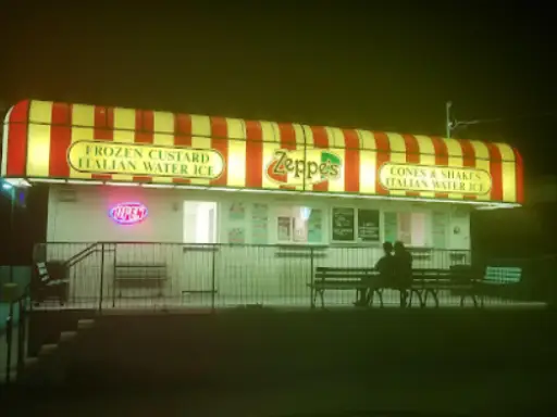 Two people relax outside an ice cream stand at night while Rhino Rooter crews complete sewer work nearby.