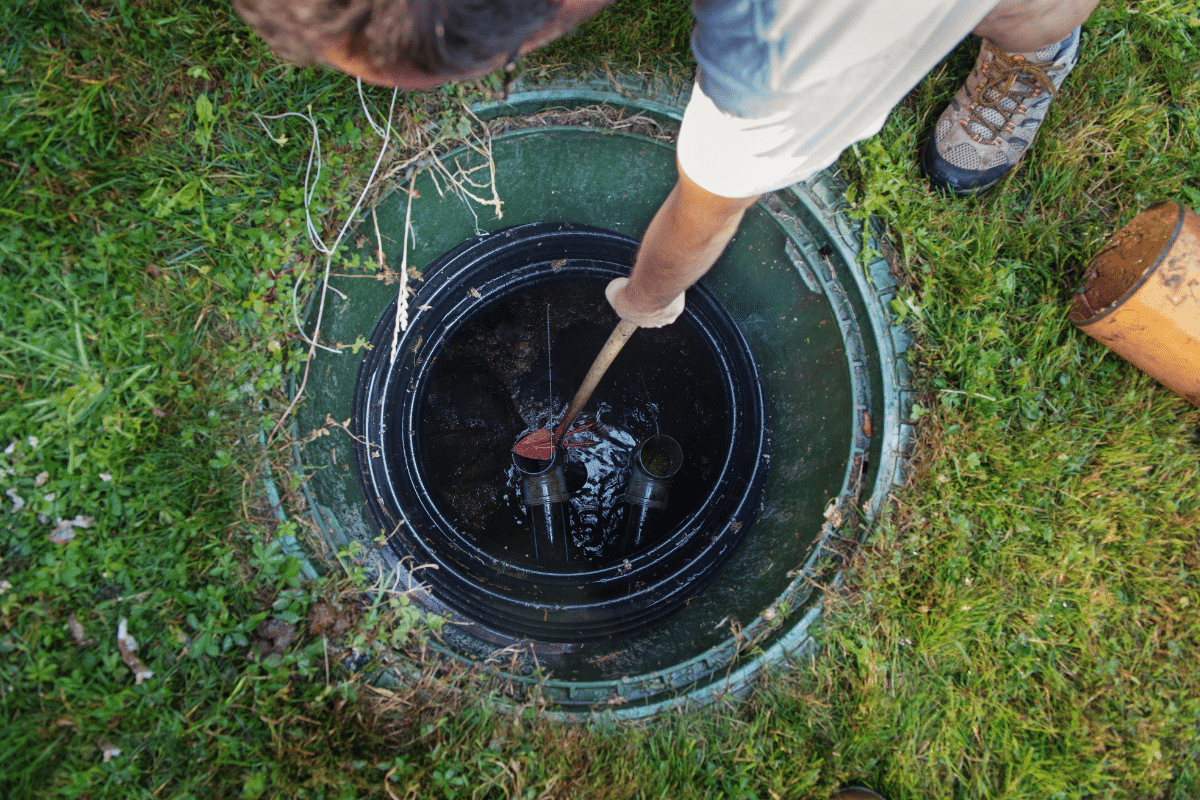 Rhino Rooter team member checks a septic tank outdoors, preparing for sewer or pipe repair.