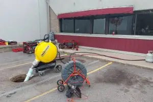 Rhino Rooter workers are cleaning a manhole with equipment in a parking lot outside a building.