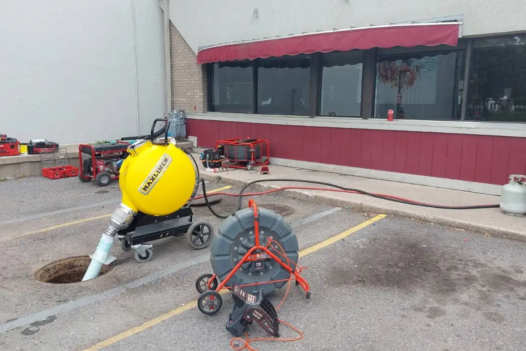 Rhino Rooter workers are cleaning a manhole with equipment in a parking lot outside a building.