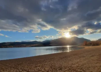 A peaceful lake sits by a sandy beach as sunlight breaks through the clouds, brightening everything. This scene shows how Rhino Rooter brings light and calm to any plumbing problem in The Wasatch Front.