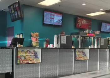 A busy theater snack counter with a friendly Rhino Rooter team member serving customers and bright menu signs showing available treats.