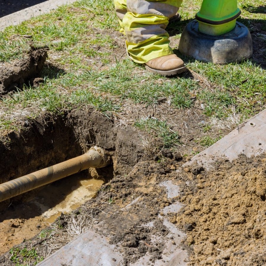 A Rhino Rooter worker stands by a dug-up pipe, prepared to replace or fix underground sewer lines.