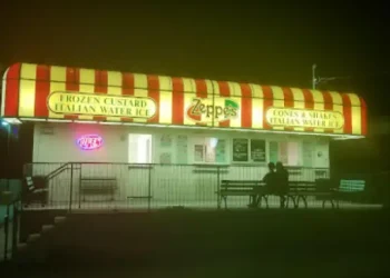 Two people relax outside an ice cream stand at night while Rhino Rooter crews complete sewer work nearby.